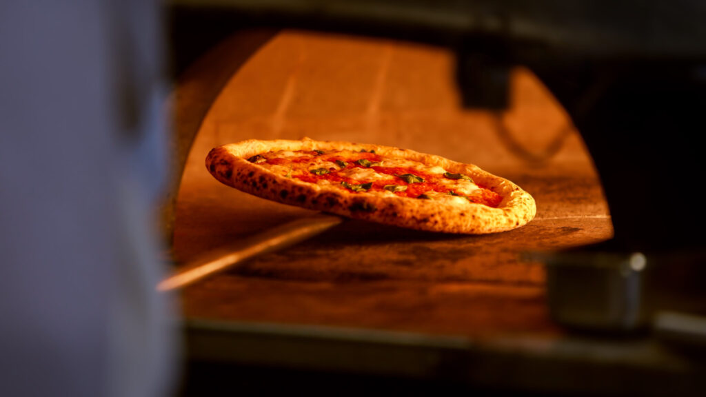 A pizza is baking on a stone in a traditional brick oven surrounded by flames
